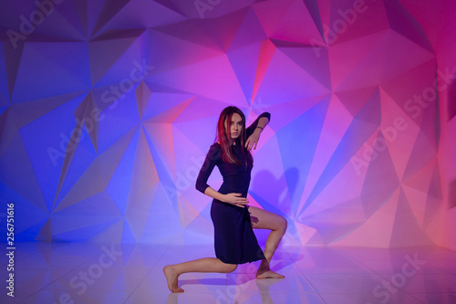 Woman dancing on the background of a beautiful multicolored wall. Sexy slim lonely girl with long black hair in a beautiful dark blue dress. bright colorful geometry background in dancing school