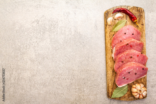 Raw pork tenderloin with vegetables and spices. Cooking meat background, fresh brisket boneless steak on stone background, top view, copy space.