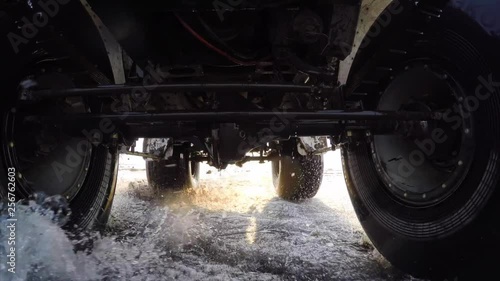 Dynamic gopro view from car bottom side. Swamp buggy is driving fast on melting snow and puddles