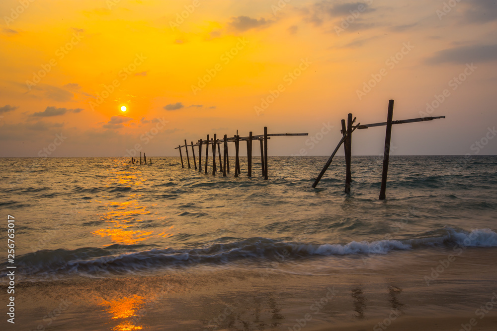 The old and broken wooden bridge on the beach with sunset