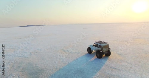 White dirty swamp buggy is driving on ice of big beautiful frozen lake Hanka in the evening. Aerial. Far East of Russia photo