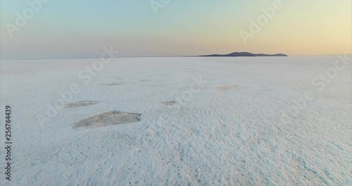 Dynamic aerial view of dirty swamp buggy driving fast on ice of big beautiful frozen lake Hanka in the evening. Far East of Russia photo