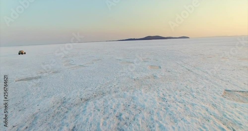 Flying above frozen lake surface, white jeep driving on ice is on the left. Aerial. Evening. Lake Hanka, Far East of Russia photo