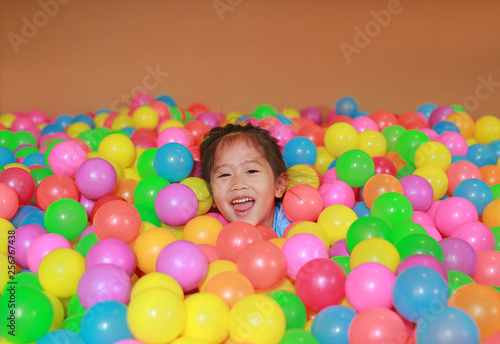 Happy little Asian child girl playing with colorful plastic balls playground.