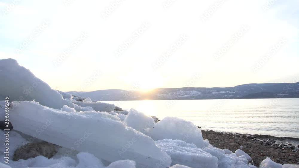 Pan to the right from a unique angle with ice in the foreground. With a beautiful sunset.