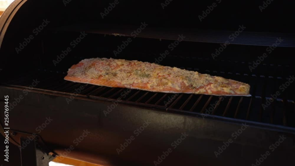 Opening the lid on a smoker checking on a Salmon fillet and allowing smoke to billow out while cooking on a wood pellet grill during the evening. Opening the lid on a smoker checking on a Salmon fillet and allowing smoke to billow out while cooking on a wood pellet grill during the evening.