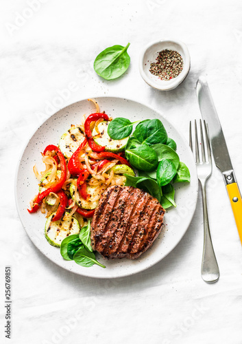 Beef steak with grilled vegetables, sweet pepper, zucchini and fresh spinach on a light background, top view. Delicious healthy balanced lunch