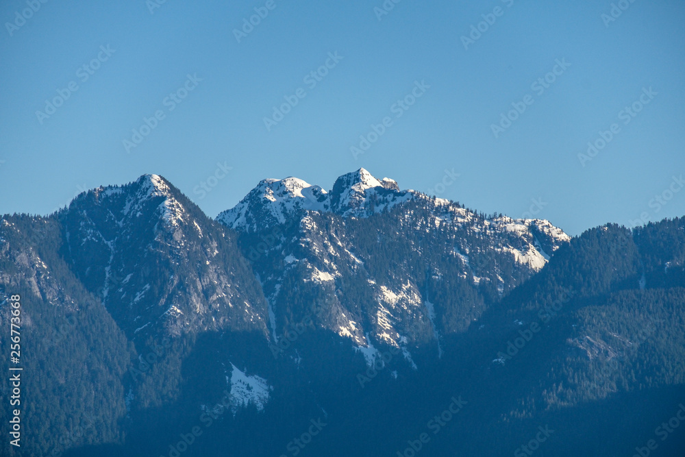 close up of snow covered mountain peaks with forest under hazy blue sky