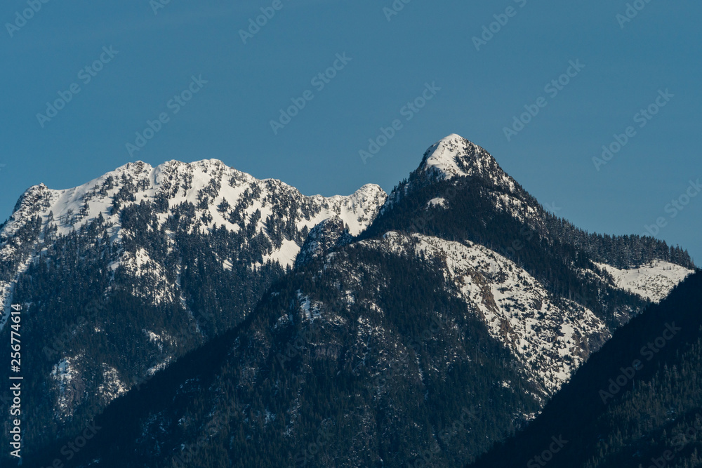 close up of snow covered mountain peaks with forest under hazy blue sky close up of snow covered mountain peaks with forest under hazy blue sky