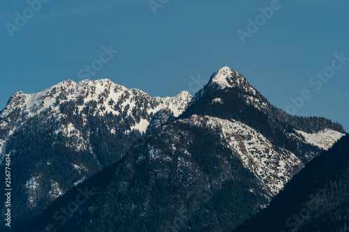 close up of snow covered mountain peaks with forest under hazy blue sky