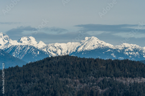 snow covered mountain range behind forest covered slope on a cloudy day