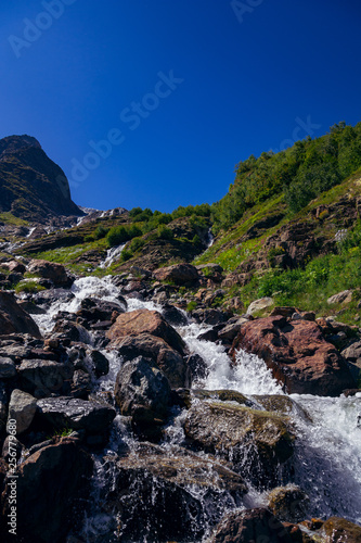 The river flows among the stones from the mountain in the surroundings of Dombai. The Caucasus Mountains on a summer, clear day. Tourie Lake.