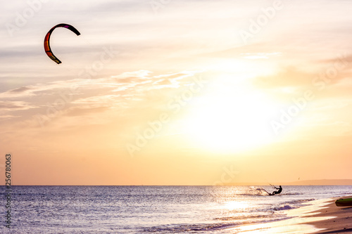 extreme professional kiter rides waves, jumps air on black sea with sail wing in hands led wind an sunset, onlookers photographers seagull on shore. village of annunciation. backlit, toned