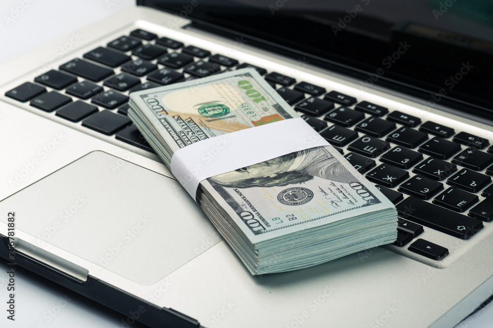 Closeup view of one hundred dollar banknotes lying on the laptop keyboard Closeup view of one hundred dollar banknotes lying on the laptop keyboard