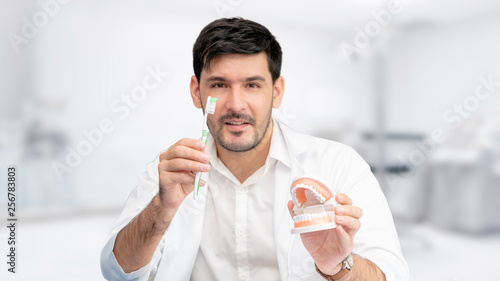 Young male dentist showing toothbrush and denture in dental clinic. Selective focus at the toothbrush. photo