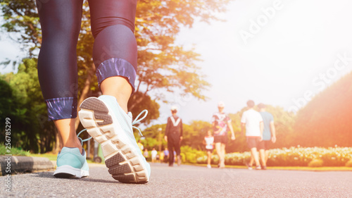 Young fitness woman legs walking with group of people exercise walking in the city public park in morning. photo