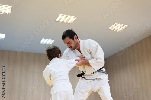 Young judoka and his father engaged in judo class in a dojo. Trainer teaches child the methods and positions of single combat, judo, karate or aikido photo