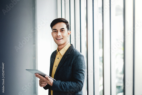 Portrait of Happy Businessman Standing by the Window in Office. Using Digital Tablet and Smiling. Looking at Camera © blacksalmon