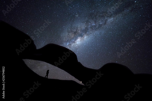A woman stands under a rock arch under the milky way photo