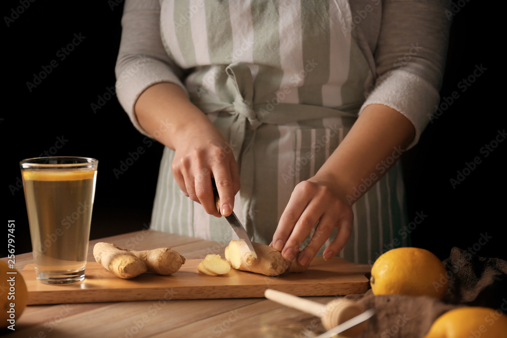 Woman cutting ginger for natural beverage on wooden table