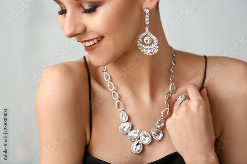 Young woman with beautiful jewelry on light background, closeup