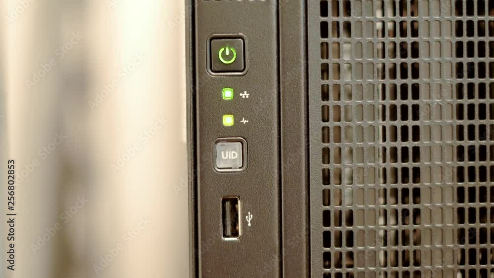A green network indicator light blinks sporadically on a black tower server. A green network indicator light blinks sporadically on a black tower server.
