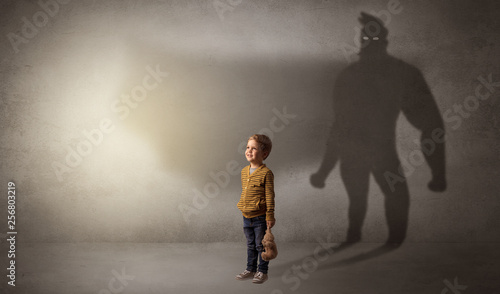 Cute kid in a room with plush on his hand and hero shadow on his background 