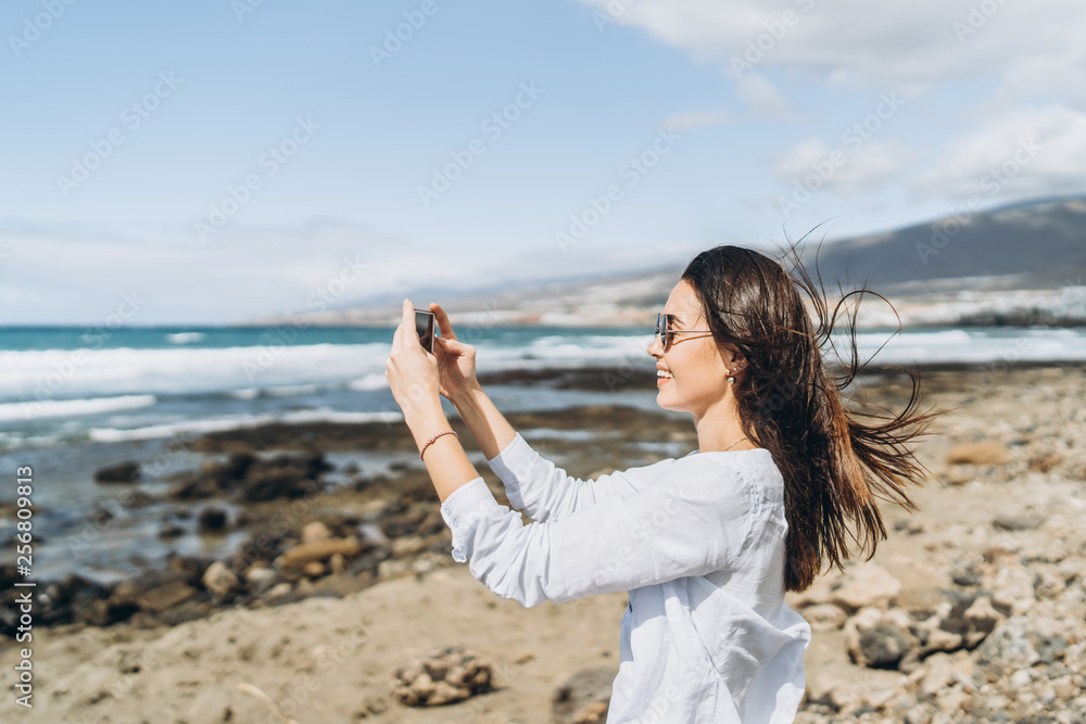 Pretty happy brunette girl with smart phone on the beach near ocean.