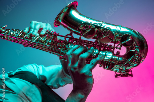 Wall Mural African American handsome jazz musician playing the saxophone in the studio on a neon background