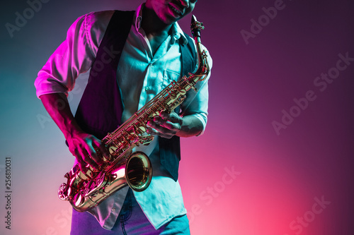 African American handsome jazz musician playing the saxophone in the studio on a neon background. Music concept. Young joyful attractive guy improvising. Close-up retro portrait. photo