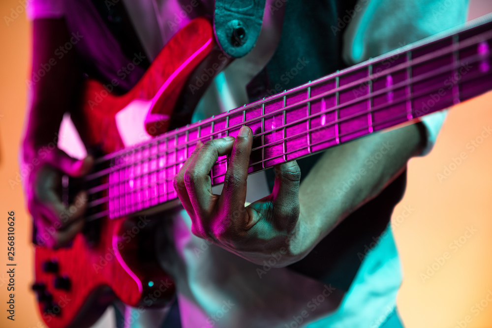 Obraz premium African American handsome jazz musician playing bass guitar in the studio on a neon background. Music concept. Young joyful attractive guy improvising. Close-up retro portrait.