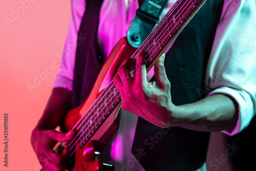 Canvas Print African American handsome jazz musician playing bass guitar in the studio on a neon background