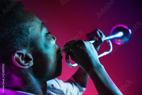 Canvas Print African American handsome jazz musician playing trumpet in the studio on a neon background