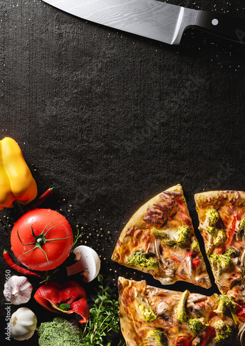 Hot Italian pizza on a black stone plate. Around are fresh tomatoes in drops of water, sweet and spicy peppers, greens, spices, salt and black pepper. Ideal for the restaurant menu or for intro video