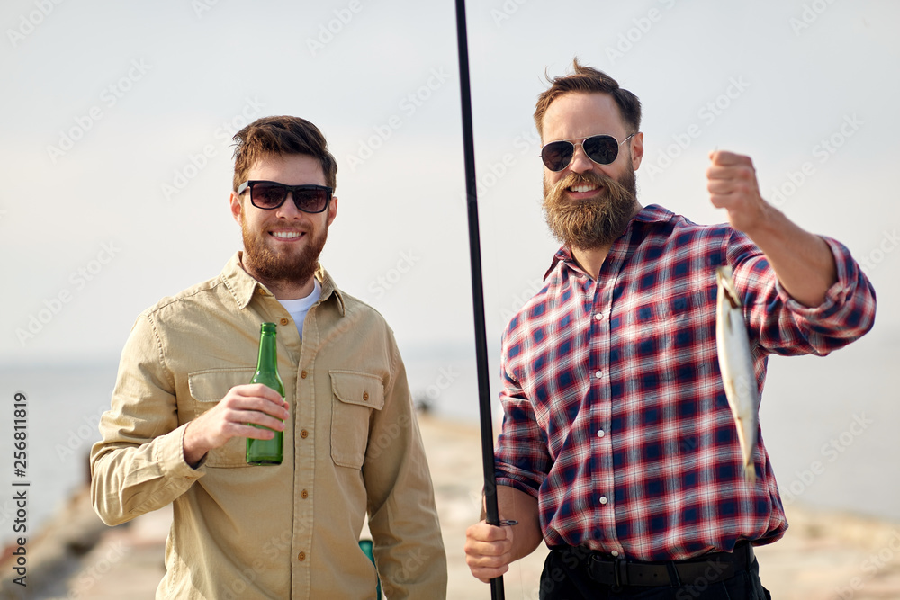 Fototapeta premium leisure and people concept - happy friends with fishing rods, fish and beer on pier at sea