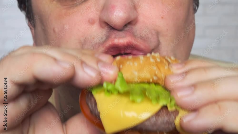 Adult man eating a nourishing hamburger. Junk food. Close-up. Adult man eating a nourishing hamburger. Junk food. Close-up.