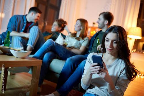 technology, internet addiction and people concept - young woman with smartphone at home friends party in evening