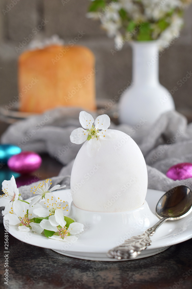 White egg and flowers on clay plate. Happy Easter card. Holidays breakfast concept. Festive table place setting decoration with blossom, bunny, chocolate eggs.