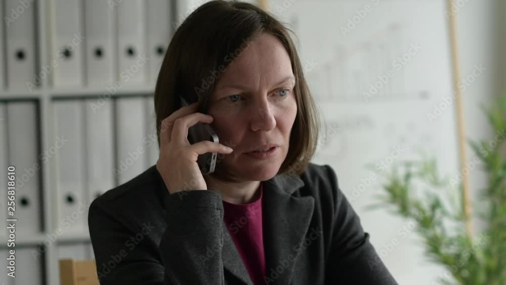 Businesswoman talking on mobile phone in business office with serious poker face expression, handheld slow motion footage Businesswoman talking on mobile phone in business office with serious poker face expression, handheld slow motion footage