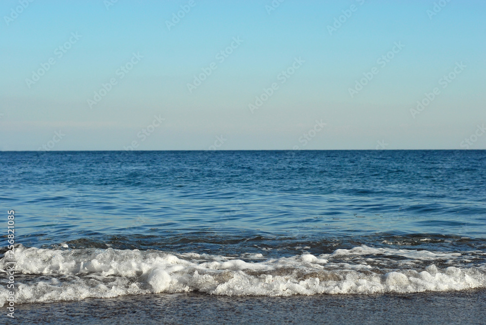 Rocky coast of the sea. Waves on the beach. Blue sea water.