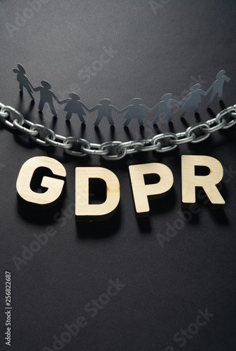 Wooden GDPR letters in front of human paper figures and metal chain. General data protection concept.