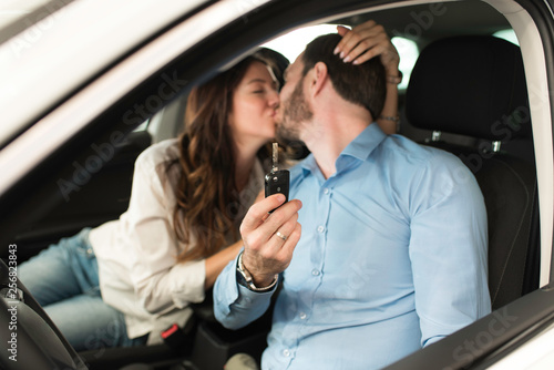 Beautiful couple sitting in a new car holding car keys and kissing each other. Buying new car concept.
