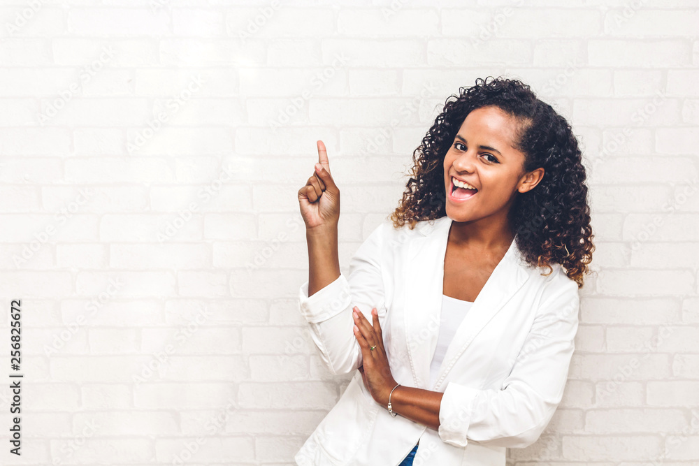 Smiling african american black woman pointing to empty copy space standing on white brick wall background Smiling african american black woman pointing to empty copy space standing on white brick wall background