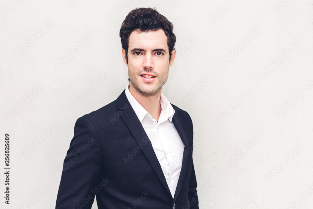 Portrait of handsome smiling businessman in black suit standing on wall background Portrait of handsome smiling businessman in black suit standing on wall background