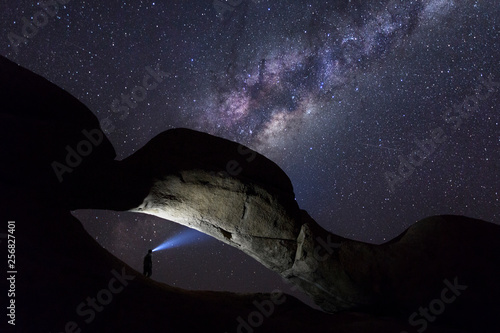 Person under a rock arch with milky way above photo