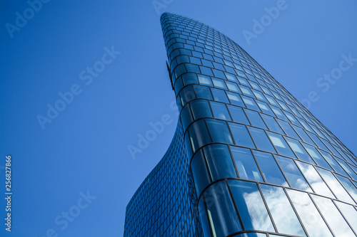 Modern architecture of office buildings. A skyscraper from glass and metal in the form of a curved wave. Reflections in windows of the blue sky and houses. Business center.