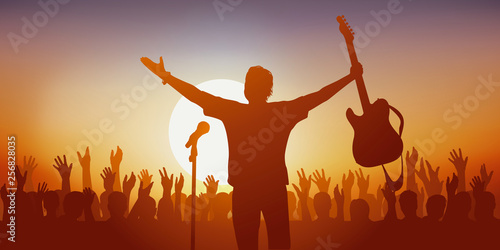 Concept du concert de musique rock avec un chanteur qui salue son public en brandissant sa guitare et la foule qui l’applaudit à la fin du spectacle.