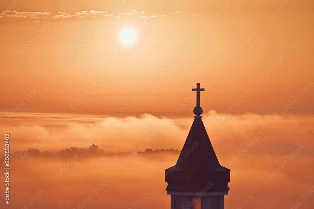 Foggy cross church sunrise morning with beautiful colours. Clouds with natural colors.