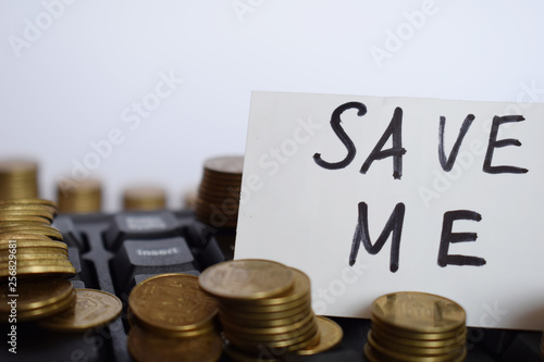 The inscription Save me on a white piece of paper on the keyboard surrounded by coins, the concept of saving money
