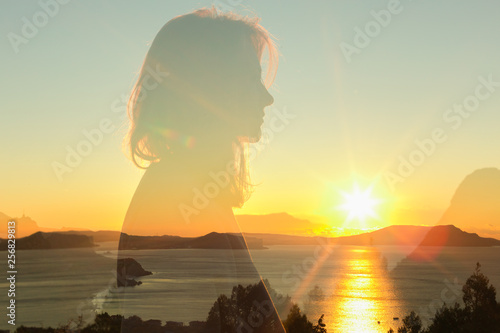 double exposure warm profile portrait of young woman wearing sweatshirt, sea , hills and sunrise on the background